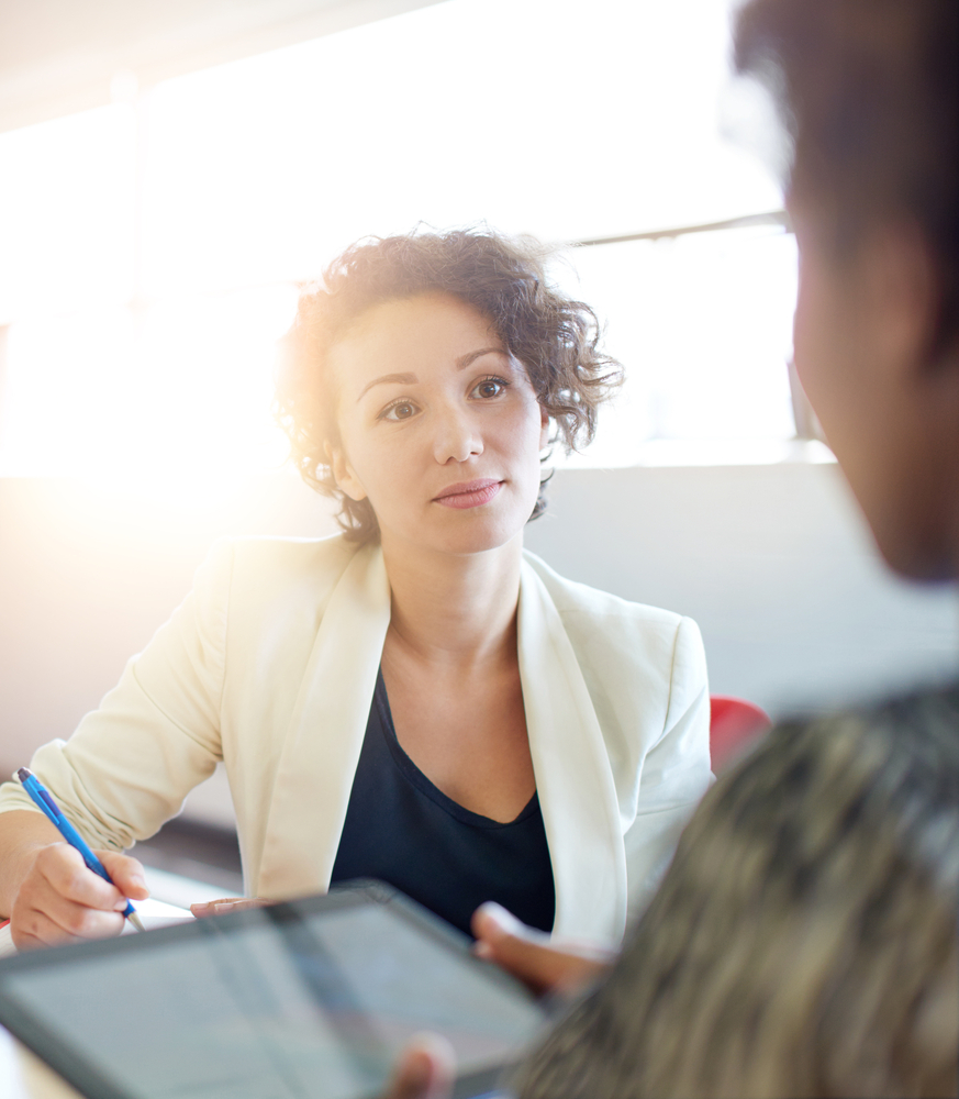 Handsome confident young businessman in glasses leaning back relaxing in his chair as he chats to a female colleague