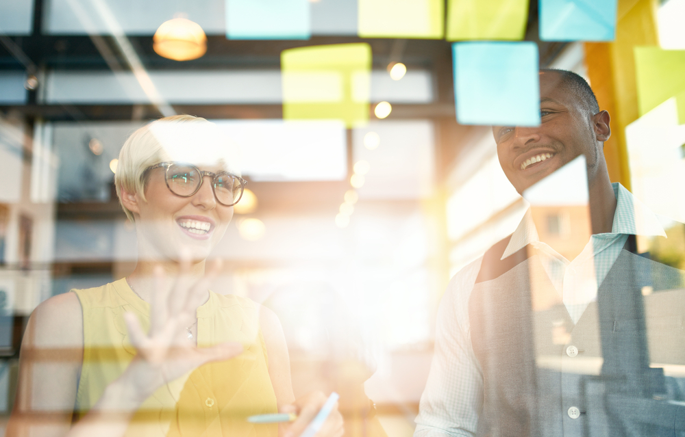 Two creative millenial small business owners working on social media strategy brainstorming using adhesive notes in windows